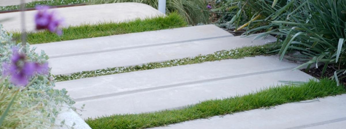 Concrete garden pavers separated by lush grass forming a path through the flowers