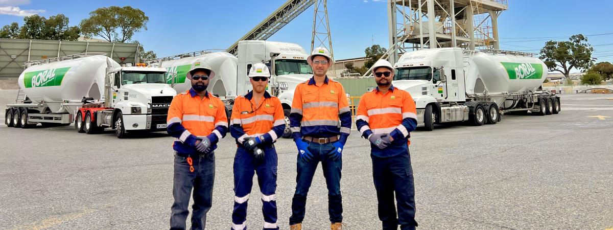 Group of staff standing in front of cement tanker trucks and a silo in the background