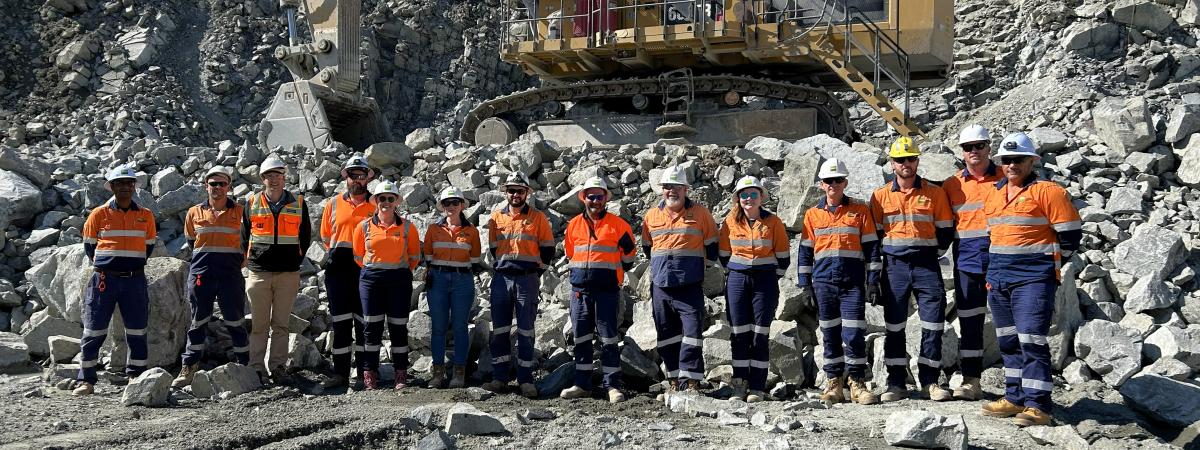 Boral team stand in quarry pit in from of CAT HME