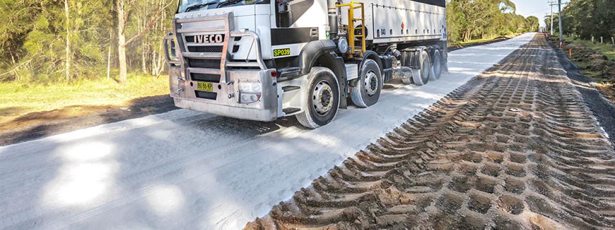 Heavy vehicle driving on dirt road with layer of white lime on top