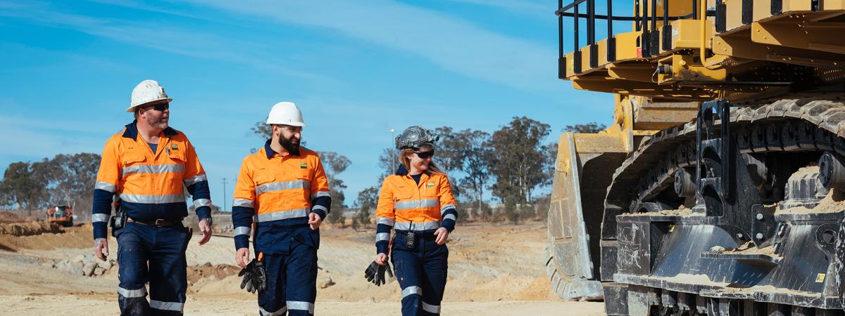 three boral staff walking on dirt road near heavy vehicle
