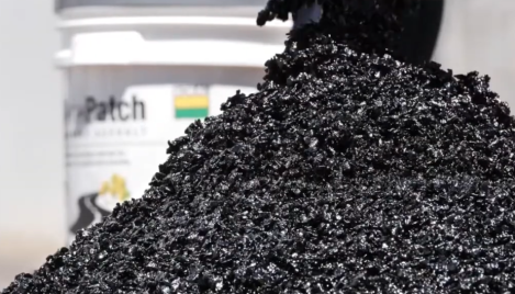Closeup of asphalt in a pile with pail in the background.