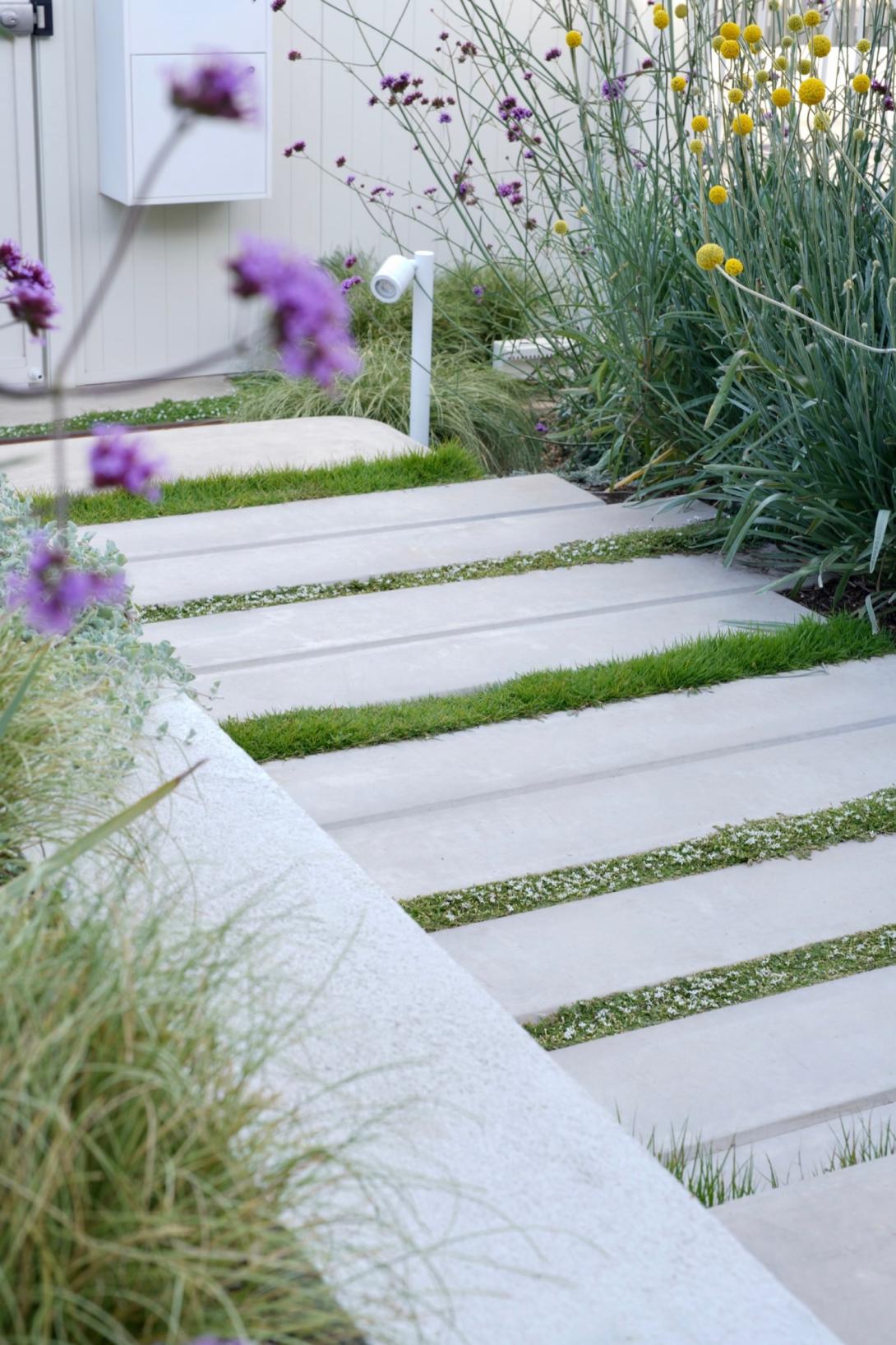 Concrete garden pavers separated by lush grass forming a path through the flowers