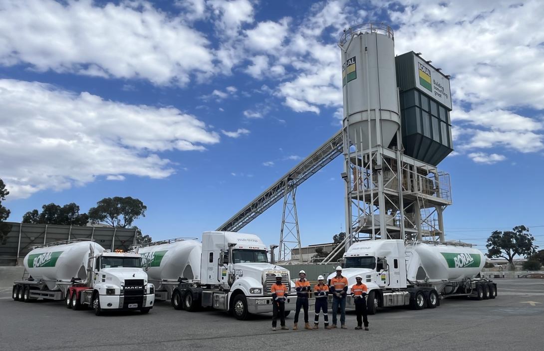Group of staff standing in front of cement tanker trucks and a silo in the background