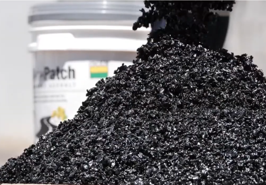 Closeup of asphalt in a pile with pail in the background.
